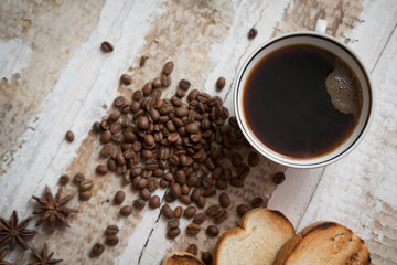 coffee cup, coffee beans of toast scattered on the rough wooden surface background