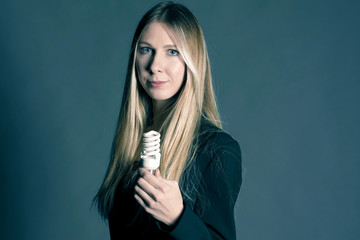 Serious young business woman holding a light bulb on a grey background. Concept of ideas and symbolization