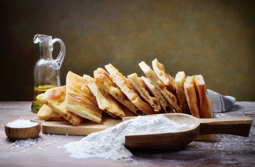 Focaccia bread, flat bread with flour, extra virgin olive oil and salt in rustic setting. Copy...
