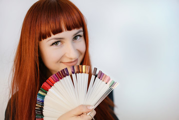 Girl with a beautiful manicure, holding in her hands samples of manicure. Portrait of a woman with red hair.