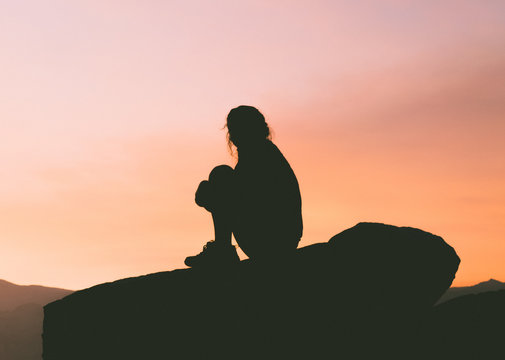 Silhouette of woman sitting on rocks at sunset