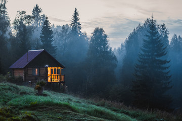  Сute rustic wooden house in the fog near the forest. Small old wooden house in foggy forest....