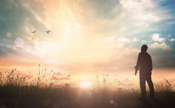 Easter Religious concept: Silhouette of human standing to worship God in meadow autumn sunset background