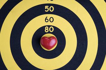 Love target background with shiny red heart shape on center of cupid archery yellow dartboard