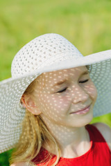 portrait of little girl with shadow on her face from white hat with large brim on green meadow background