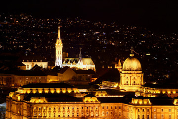 Fototapeta na wymiar Closeup evening view of Buda Castle World Heritage Site with Baroque Royal Palace, Gothic Matyas Church, lit by exterior lights, and light dots of built-up hills Budapest Hungarian capital city Europe