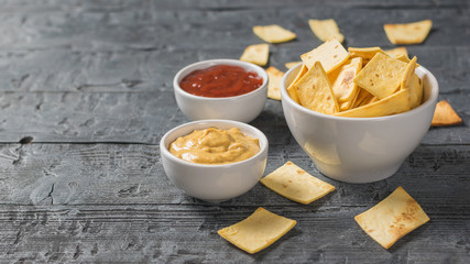 Mexican tortilla chips in a bowl with sauce and mustard on the table.