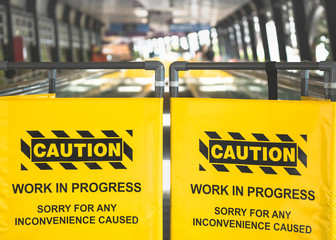 yellow sign of working area caution, black copy print on vinyl, blurred close walkway as background