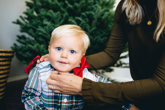 Millenial mom putting a red bow tie on her one year-old son