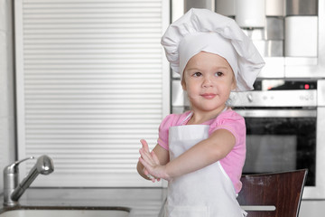 Little girl making dough and cookies in kitchen