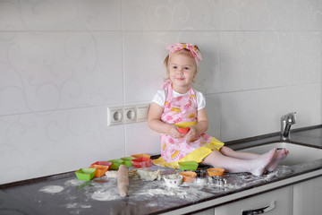 Little girl making dough and cookies in kitchen