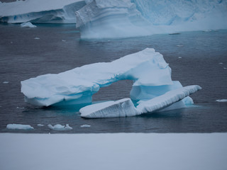 A Smalled Arched Iceberg pale blue and light turquoise blue floating in the dark gray water of the Southern Ocean in Antarctica.