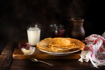 Pancakes with jam, butter and milk in a ceramic pot
