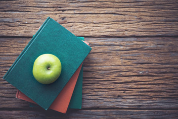 Green apple on books with wooden background.
