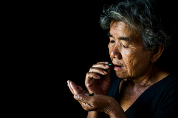 Old woman take a pill on black background, concept illness and healthcare