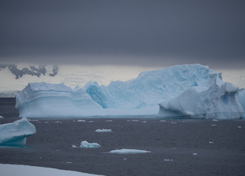 Light turquoise blue iceberg in Charlotte Bay Antarctica. Thick gray clouds are overhead and the steel blue water of the Southern Ocean in the foreground.