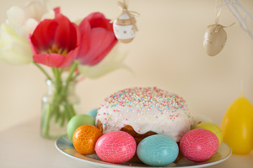 Easter cake with colored eggs,tulip flowers and twig with decorative  Easter eggs on a beige background.Easter food. Easter composition.
