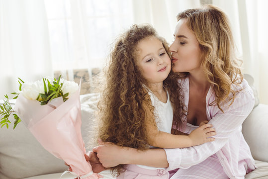 happy mom kissing her daughter and holding bouquet of flowers for happy mothers day