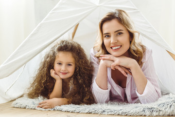 smiling mom and happy curly daughter lying in kid wigwam © LIGHTFIELD STUDIOS