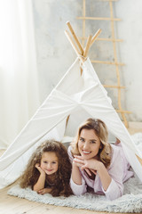 beautiful cheerful mother and curly daughter lying in kid wigwam © LIGHTFIELD STUDIOS