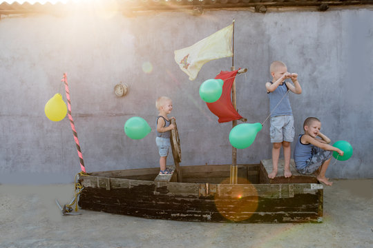 Happy boys play pirates and seafarers. Three brothers have fun together. The old boat is decorated with balloons.