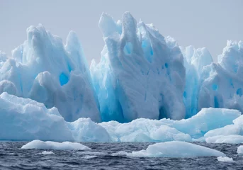 Rolgordijnen Blauwe ijsberg drijvend in Esperanza op Antarctica met kloven, spleten en holtes. © tloventures