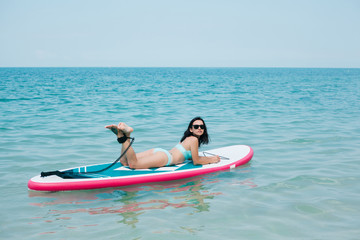 attractive slim girl lying on paddle board on sea at tropical resort