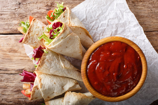 Freshly cooked burritos with turkey, lettuce and vegetables close up on a paper. horizontal top view