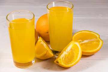 Glass of orange juice and fresh oranges on white wooden table