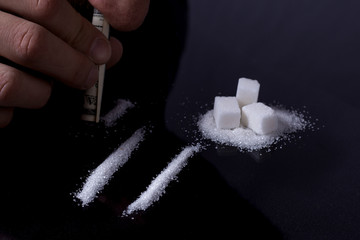 Sugar addict. Addiction of sweets and fast carbohydrates. A line of white sugar sniffs a man through the dollar like cocaine. Dark background