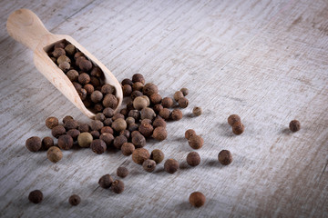 Pepper peas in a wooden spoon on a wooden background. Spices are scattered on the table
