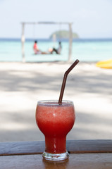 watermelon smoothie  on wooden table with happy couple on swing  background.  Lipe island,Thailand