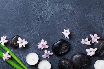 Obraz na płótnie Canvas Spa background with massage pebble, green leaves, beautiful flowers and candles on black stone table top view. Aromatherapy, relaxation and zen like concept.