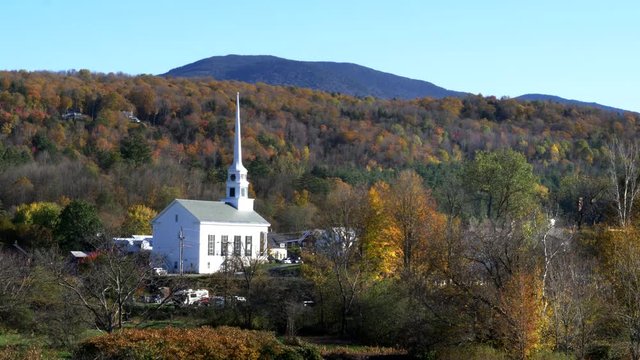 a classic new england white church at stowe and a hill covered with fall foliage in vermont, usa