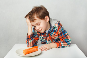 boy in plaid shirt sitting in front of a plate with carrots