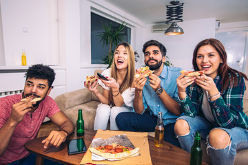 Group of young friends eating pizza and watching tv.Home party.Fast food concept.