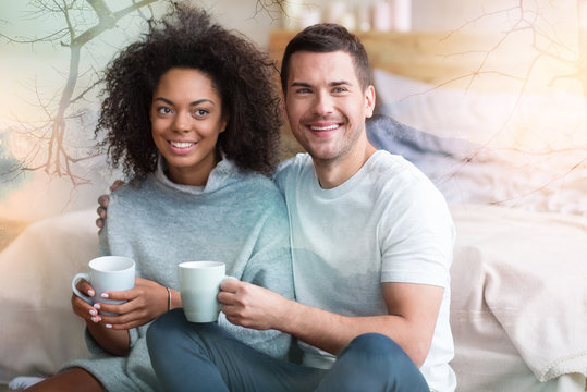 Pretty couple. Joyful pretty nice couple sitting together and smiling while holding cups with tea