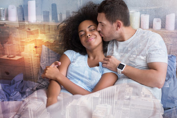 Morning kiss. Positive handsome delighted man closing his eyes and kissing his girlfriend while cuddling together with her in bed