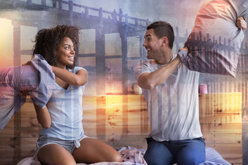 Having fun. Positive joyful nice couple holding pillows and laughing while fighting with them