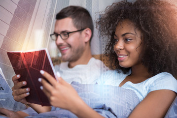 Interesting story. Joyful nice smart woman holding a book and smiling while reading it
