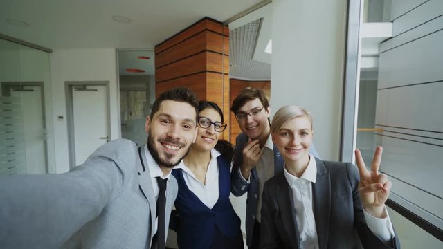 POV of Happy business team taking selfie portrait on smartphone camera and posing for group photo during meeting in modern office