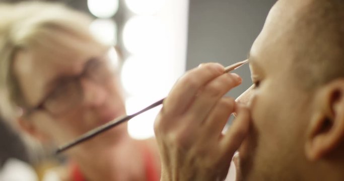 4K Close up professional makeup artist preparing handsome man backstage. Slow motion.