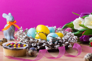 Easter blue and yellow eggs in the nest, cupcake, easter rabbit and tulips. Easter background with colorful tulips.