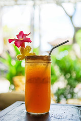 Orange ice tea on a wooden table with a metal tube and a flower. Lemonade with ice. Side view with copy space