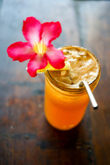 Orange ice tea on a wooden table with a metal tube and a flower. Lemonade with ice. Top view with copy space