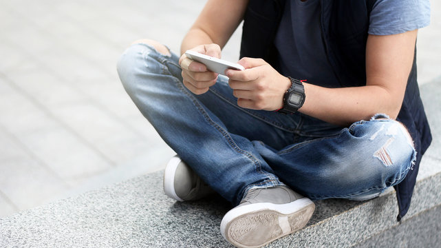 A young guy uses his smartphone while sitting on the asphalt.