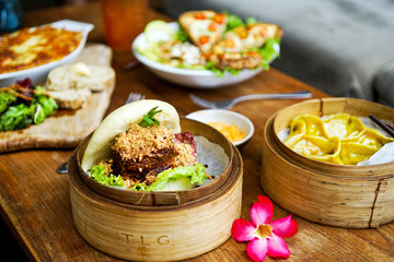 Raclette Tartiflette and salad Chevre Chaud - french kitchen.  Bao burger and Asparagus tofu dumpling - Chinese kitchen. Side view in cafe.