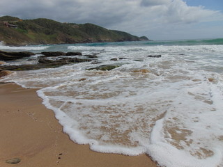 espuma de mar blanca llegando a la arena dorada de playa desierta con montañas y cielo