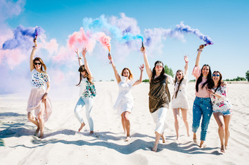 Beautiful happy stylish sexy young girls stand beach and hold light up colored smoke bombs. burn...
