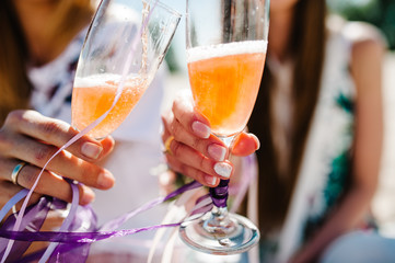 Hands of girls with boutonnieres, ribbons, flowers in foreground hold, raise glass of champagne up on background  stylish girls. Party in Style boho. Maiden evening Hen-parties. Bachelorette. Close up